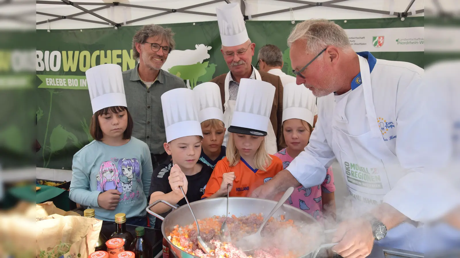 Die Viertklässler rühren fleißig im Topf, während (v.l.) Harald Nutt und stellv. Bürgermeister Detlef Gehle über die Schultern schauen und Spitzenkoch Markus Haxter geduldig anleitet. (Foto: Marc Otto)